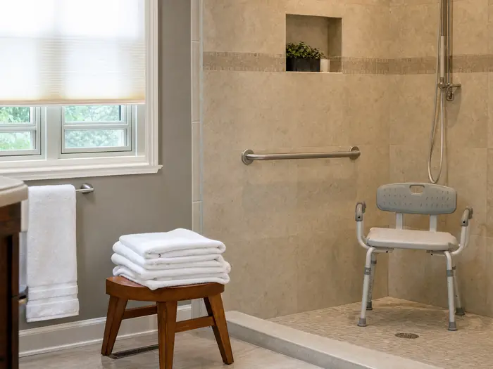 A safe walk-in shower with a grab bar, shower chair and folded towels
